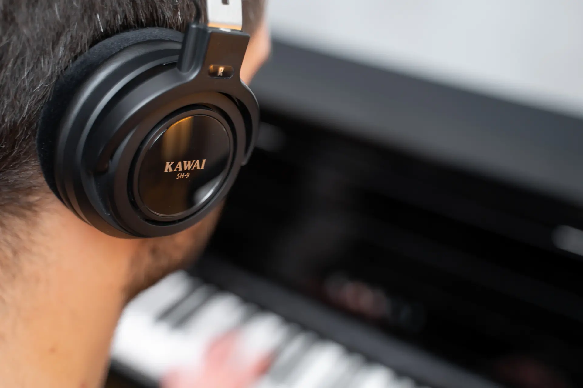 A person wears Kawai headphones while playing a digital piano.