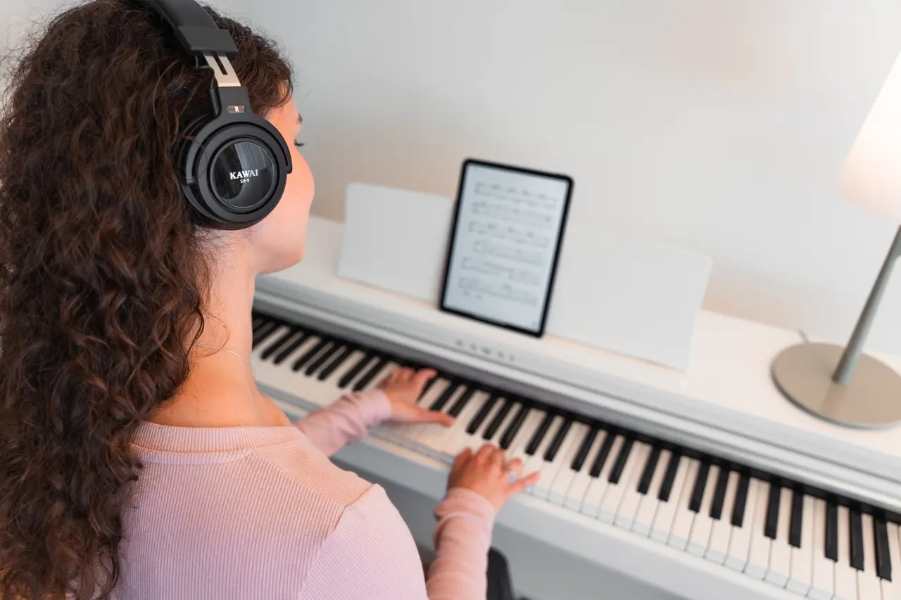 Junge Frau mit Kopfhörern spielt an einem weißen Kawai CX Digitalpiano