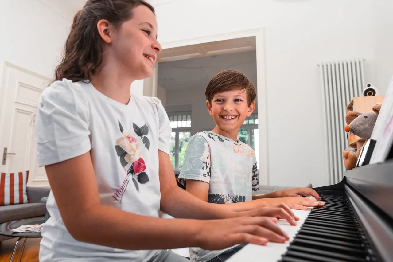 Frau und Junge sitzen lächelnd gemeinsam an einem Digitalpiano.
