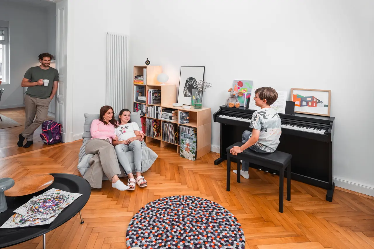 Familie im Wohnzimmer, während ein Kind auf einem schwarzen Kawai Digitalpiano spielt.