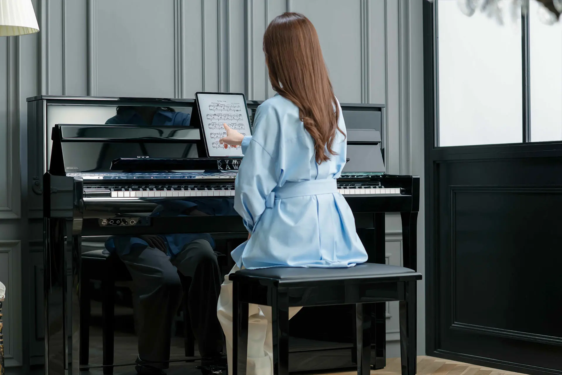 Femme assise devant le piano hybride Kawai NOVUS et tenant une tablette