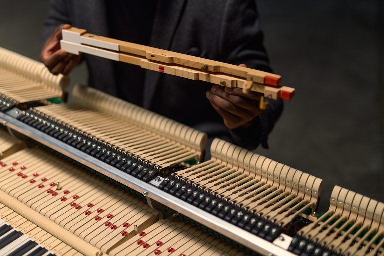 Hände halten eine verlängerte Kawai Tastenmechanik über dem geöffneten Piano