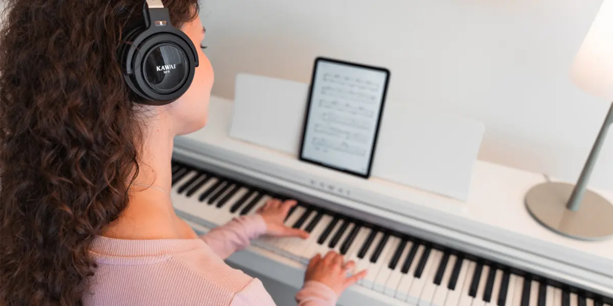 Person mit Kopfhörern spielt auf einem Kawai CX102 Digitalpiano mit Notenanzeige auf einem Tablet