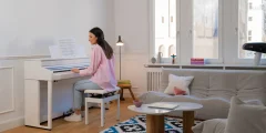 Une femme joue sur un piano numérique Kawai CA501 blanc dans un salon lumineux