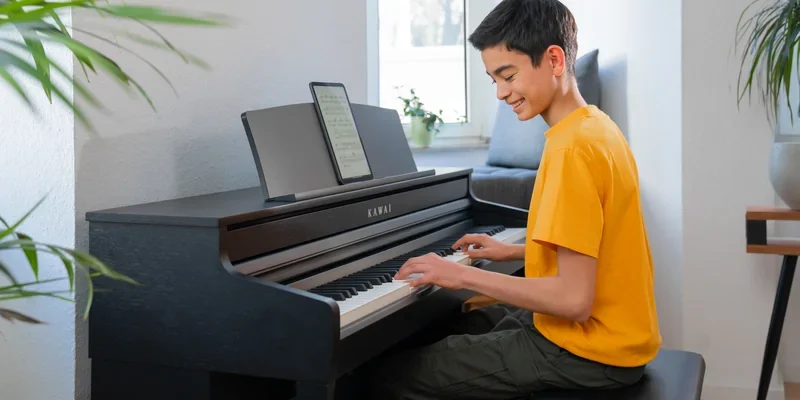 Jugendlicher uebt an einem Kawai CA Digitalpiano mit Noten auf dem Display
