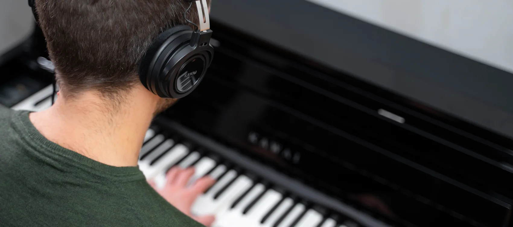 Pianist mit Kopfhoerern an einem schwarzen Kawai CA Digitalpiano von hinten